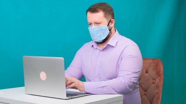 Side view portrait of a cheerful brunette man with surgical medical mask working on email laptop typing or chatting in social. - Φωτογραφία, εικόνα