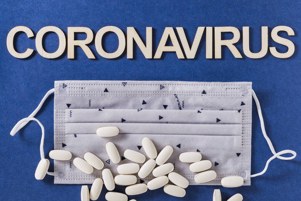 Słowo koronawirus z drewnianymi literami, maską ochronną twarzy i tabletkami skompresowanymi, na niebieskim tle - Zdjęcie, obraz