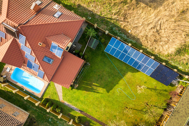 Vista aérea de uma casa privada com jardim coberto de grama verde, painéis solares no telhado, piscina com água azul e gerador de turbinas eólicas. - Foto, Imagem