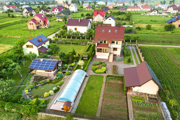 Vista aérea de uma casa privada no verão com painéis solares fotovoltaicos azuis na parte superior do telhado e pátio verde
. - Foto, Imagem