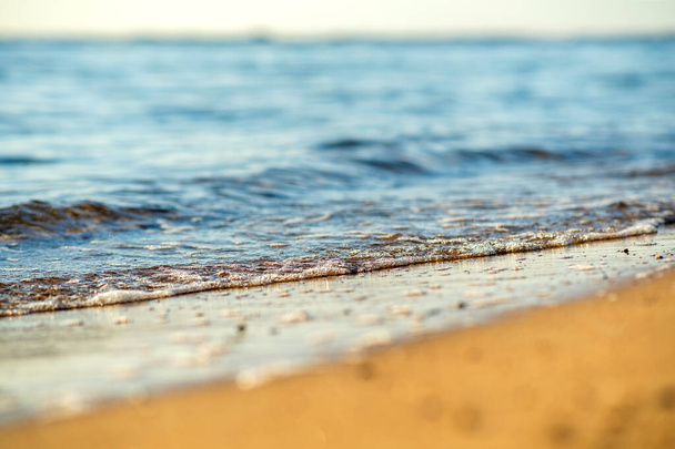 夏の晴れた海岸で黄色の砂のビーチの上に澄んだ青い水と小さな海の波の終わり. - 写真・画像