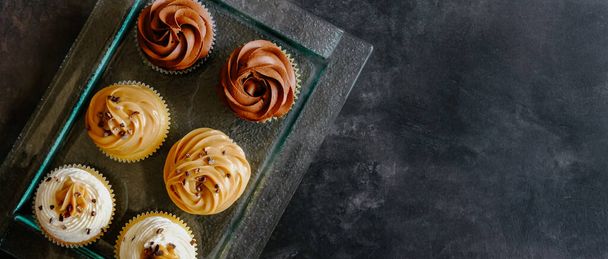 Vanilla, chocolate and caramel cupcakes on wooden table background. Sweet food concept.  - Фото, изображение