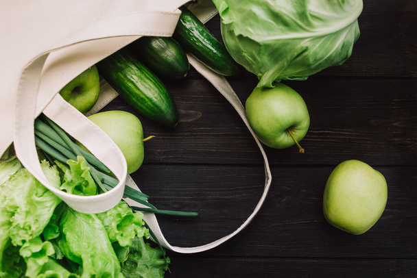Taze yeşil sebzeler ve meyve torbası. Salatalık, lahana, marul, elma ve otlar siyah ahşap arka planda. Detoks ve yeşil diyet. Sağlıklı yaşam tarzı kavramı. Çevre yaşamı - Fotoğraf, Görsel