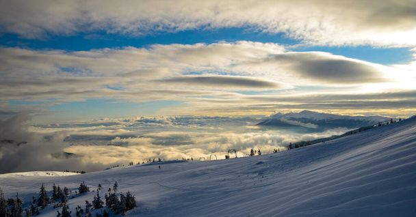 Воздушный вид над облаками на горных вершинах, покрытых снегом, освещенный солнцем
 - Фото, изображение