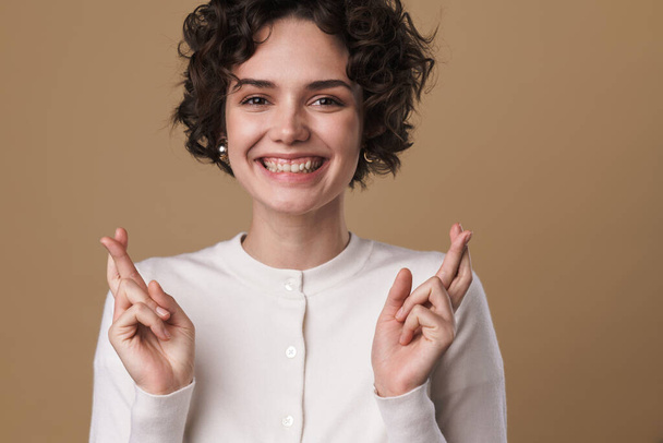 Image of smiling beautiful woman holding fingers crossed foe good luck isolated over beige background - Fotoğraf, Görsel