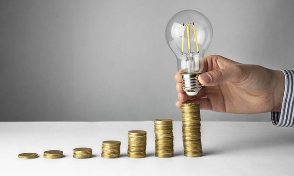 Bedrijfsconcept. Een hand houdt een lamp boven munten op een lichte achtergrond. Zakelijke ideeën, brainstormen. Herstel en bedrijfsgroei. Kopieerruimte - Foto, afbeelding