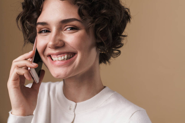 Image of joyful beautiful woman laughing and talking on cellphone isolated over beige background - Foto, Bild