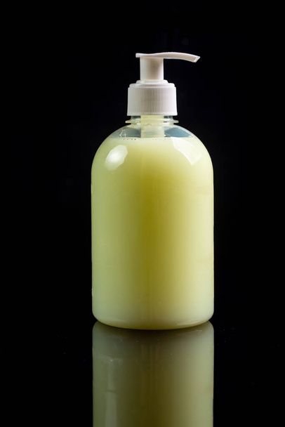 Κίτρινο αντισηπτικό υγρό σαπούνι σε ένα μπουκάλι με ένα δοχείο σε μαύρο φόντο. Πλευρική άποψη, κοντινό πλάνο. Κατακόρυφος προσανατολισμός. - Φωτογραφία, εικόνα