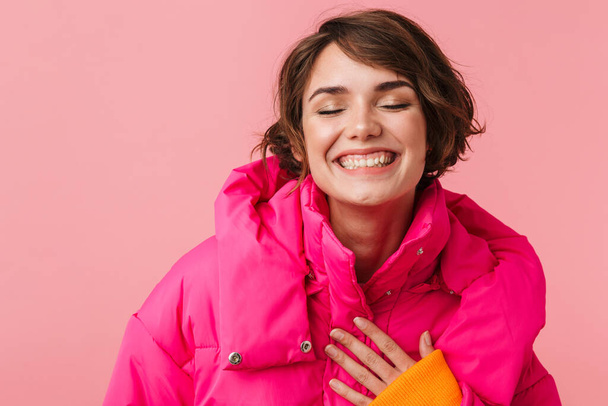 Portrait of funny caucasian woman in warm coat laughing at camera isolated over pink background - Foto, Imagem