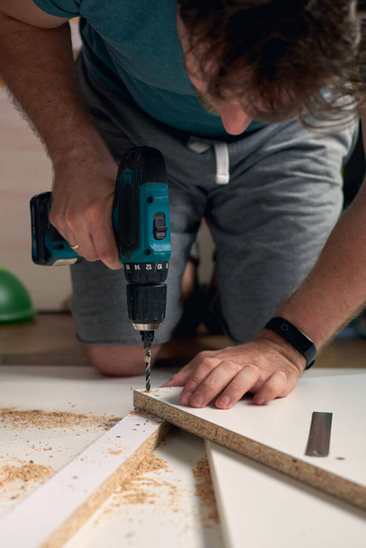 Ο άνθρωπος κάνει εργασίες ανακαίνισης στο σπίτι, γεώτρηση με ένα κατσαβίδι. Ομάδα εργαλείων επισκευής σε ξύλινο λευκό φόντο με χώρο αντιγραφής. Καινούρια ιδέα επίπλων σπιτιού. Έννοια συντήρησης επισκευής. - Φωτογραφία, εικόνα