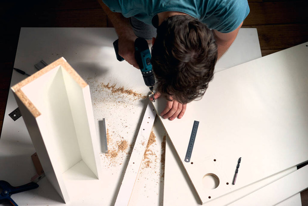 Man doing renovation work at home, drilling with a screwdriver. Group of repair tools on wooden white background with copy space. New house furniture concept. Repair maintenance concept. - Fotoğraf, Görsel