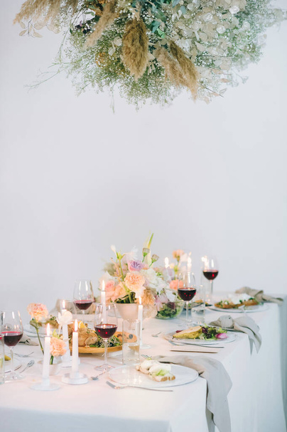 святковий стіл з квітковим букетом, свічками, винами, продуктами харчування і гірляндою з сухих квітів і листя
 - Фото, зображення