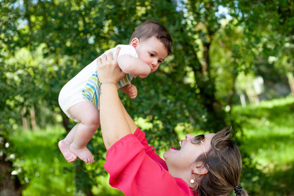 笑顔のお母さんが公園で赤ん坊を抱えている。素晴らしいコピースペース. - 写真・画像