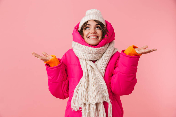 Portrait of beautiful happy woman in warm clothes smiling with trowing up hands isolated over pink background - Foto, Imagen