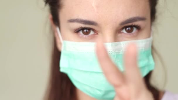 woman putting on surgical mask for corona virus prevention. Close-up of a young woman in a protective medical mask, she looks directly - Filmagem, Vídeo