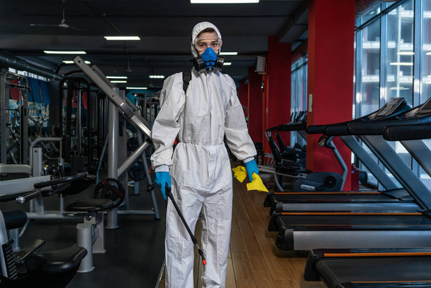 Cleaning and Disinfection in crowded places amid the coronavirus epidemic Gym cleaning and disinfection Infection prevention and control of epidemic. Protective suit and mask and spray bag - Photo, image