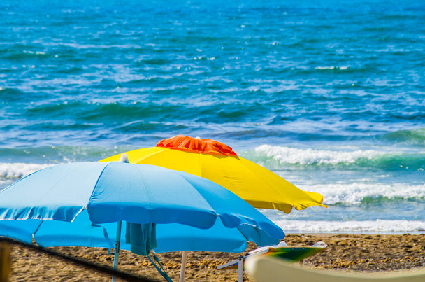 amarelo e branco e azul guarda-chuvas com o mar azul no fundo, três cores símbolos de verão como pinturas
 - Foto, Imagem