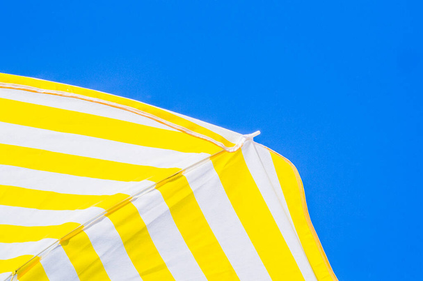 κίτρινες και άσπρες ομπρέλες με φόντο τον γαλάζιο ουρανό, τρία χρώματα σύμβολα του καλοκαιριού σαν ζωγραφιές - Φωτογραφία, εικόνα