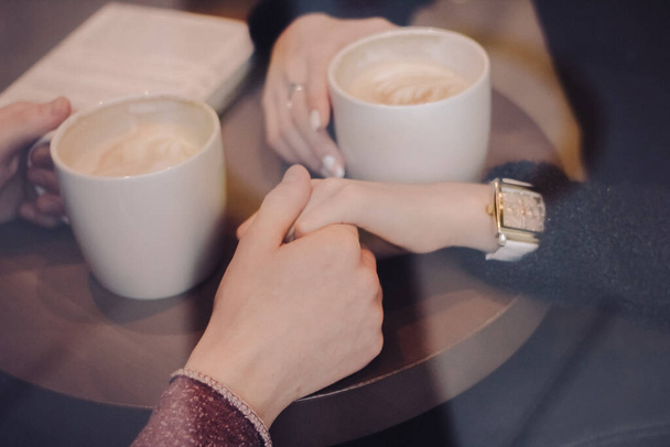 Мила брюнетка любляча пара в затишних теплих светрах на побаченні в кафе, дивлячись на телефон, використовуючи його. холодна осінь, зима або весняний день, європейське місто. в приміщенні
 - Фото, зображення