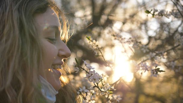 menina em uma máscara médica cheira uma árvore de floração ao pôr do sol close-up
 - Foto, Imagem