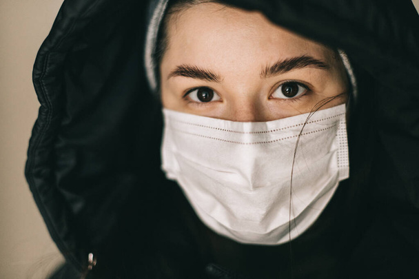 selective focus, noise effect: look of a girl dressed in a medical mask and a hooded jacket - Foto, imagen