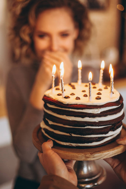 young attractive blond girl with gorgeous model smile holds cake. Emotions of a happy birthday girl from an unexpected gift: homemade cake with burning candles, selective focus, noise effect - Фото, изображение