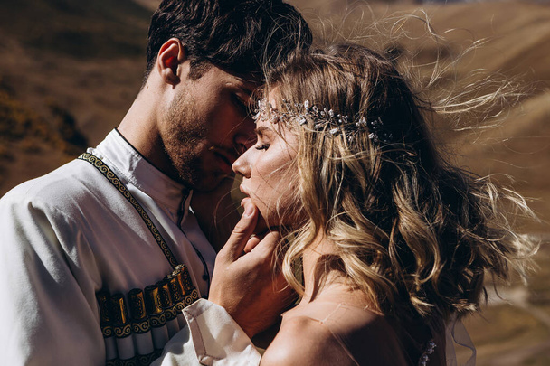 Stunning sensual outdoor portrait of young stylish wedding couple posing in summer sunset: luxury couple kissing and embracing on the mountain with incredible landscape - Fotó, kép