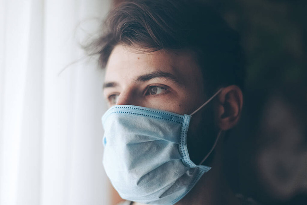 man in quarantine for Coronavirus wearing protective mask and looks out the window - Foto, Imagem