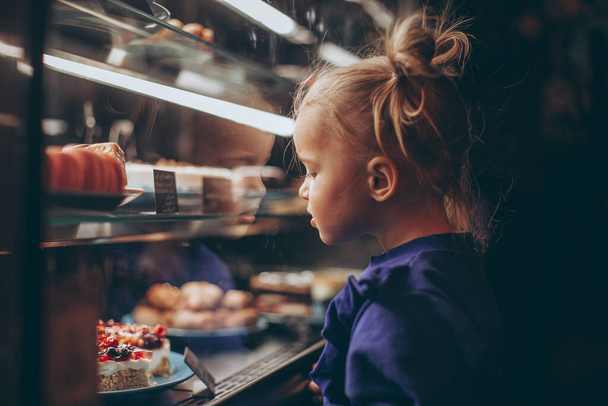 little pretty girl chooses pastries in a cafe. a child next to a showcase with goods - Fotografie, Obrázek