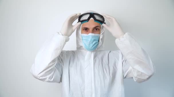 Disinfector puts on safety glasses. Virologist in protective coverall and mask working in office building - Video