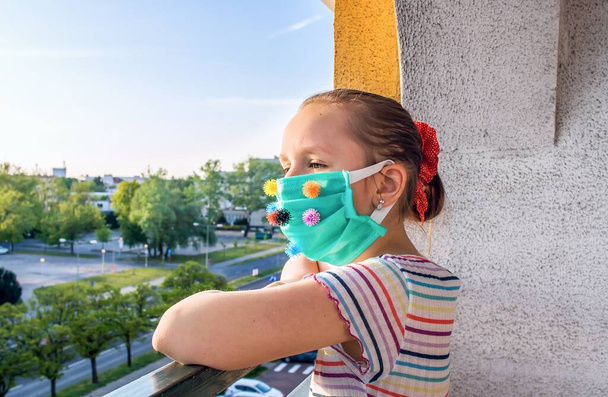 A child in a medical mask looks at an empty street near the house . pandemic background. people wait for vaccine - Photo, Image