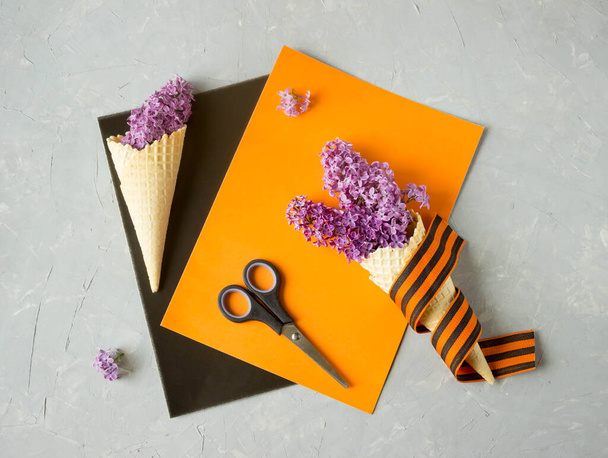 colored paper, scissors, lilac flowers and St. George's ribbon are on the table, top view, the concept of making paper crafts for the victory day holiday, may 9 - Fotó, kép