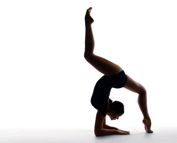 Professional female gymnast in sportswear performs a handstand. Training, elements of gymnastics, acrobatics on a white background. Sports motivation, stretching, splits. Banner for advertising - 写真・画像