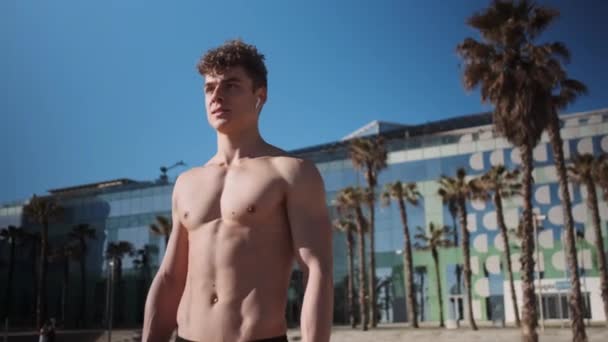 Tracking in shot of attractive fit guy resting after workout outdoor - Video, Çekim