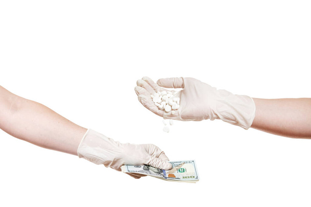 koncepcja na temat korupcji w medycynie i przemyśle farmaceutycznym łapówki, ręce w sterylnych rękawic medycznych, jedna ręka daje pieniądze, z drugiej strony leje tabletki izolowane na białym tle. - Zdjęcie, obraz