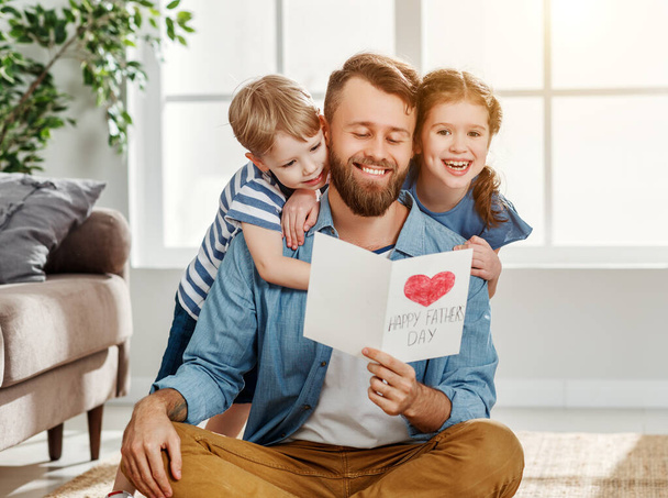 Cheerful little boy and girl congratulating happy dad with Fathers day and giving handmade greeting card while spending holiday together at hom - Фото, зображення