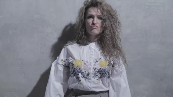 The young beautiful woman with curly hair poses, wriggles and flirts in front of a camera, close up, a grey background, is dancing, she coquets, Different emotions on a face - Metraje, vídeo