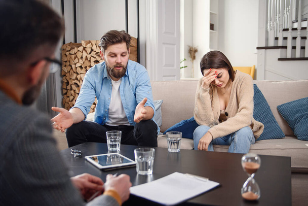 Annoyed caucasian couple of man and woman having conversation with psychologist on therapy session in light room. - Photo, Image
