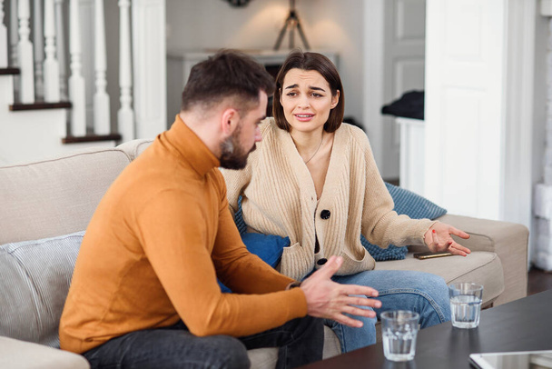 Angry couple having argument or breakup. Young husband and wife having quarrel while sitting on a couch in the living room in a big house. Infidelity concept. - Photo, Image