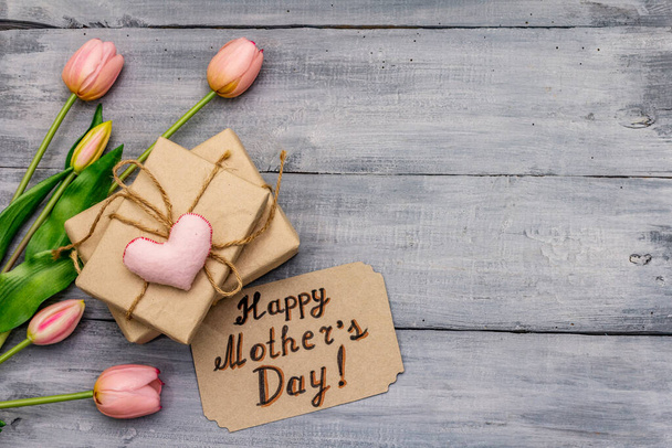 Ευχετήρια κάρτα για την Ημέρα Ευτυχισμένων Μητέρων. Απαλές ροζ τουλίπες, χειροποίητη καρδιά τσόχας, μηδενικό δώρο συσκευασίας απορριμμάτων. Ξύλινες πλάκες - Φωτογραφία, εικόνα