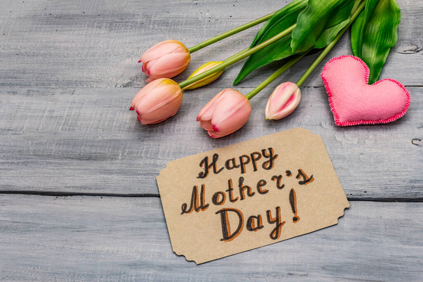 Glückwunschkarte zum Muttertag. Sanfte rosa Tulpen, handgemachtes Filzherz, kein Verpackungsmüll. Holzbretter Hintergrund - Foto, Bild