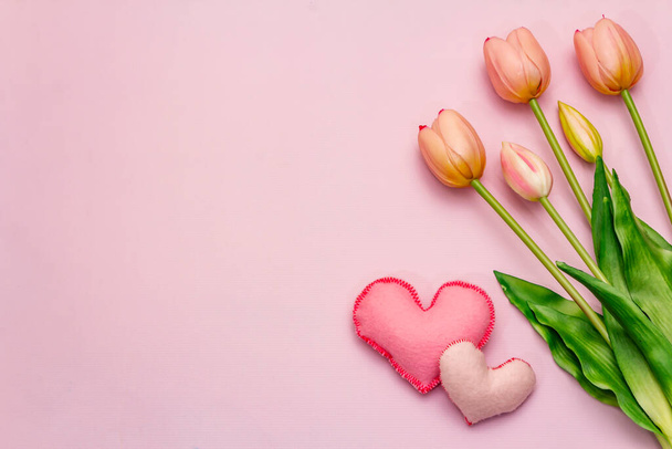 Wenskaart, behang, achtergrond. Gelukkige Moederdag, Pasen, Sint Valentijnsdag of Bruiloft. Zachte roze tulpen, handgemaakte vilten hartjes op een rooskleurige achtergrond - Foto, afbeelding