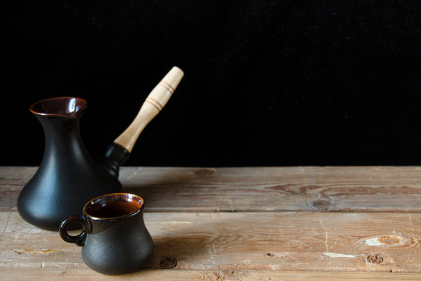 One black cup for coffee and black turk on the old wooden table and black background, place for text. Sweet home - Photo, Image