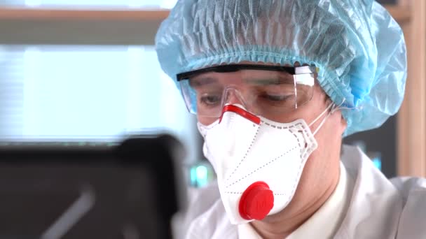 Dokter in een ademhalingsapparaat, bril en medisch masker kijkt naar de camera, dichtbij een doktersogen. Droevige en zieke dokter. De diagnose van het coronavirus COVID-19 - Video
