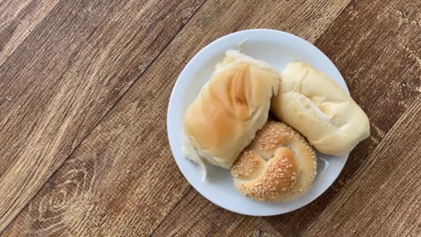 Různé chleby (francouzský, sezamový, sladký bochník) v malém talíři nad dřevěným stolem - Záběry, video