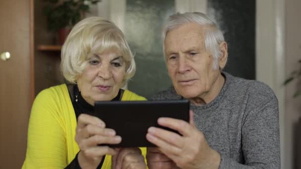 Pěkný starší pár prarodiče užívají online nakupování na tabletu doma - Záběry, video