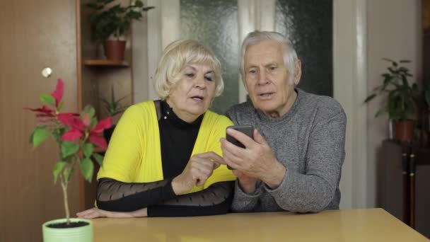 Pretty mature senior couple grandparents enjoy online shopping on phone at home - Záběry, video