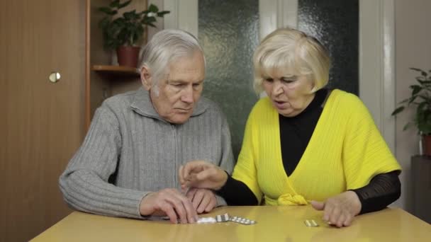 Az öreg nagyszülők tablettákat nézegetnek, tablettákat hólyagokban az asztalon otthon. - Felvétel, videó
