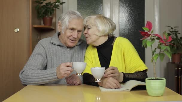 Happy old grandparents couple sit on table at home enjoy drinking tea together - Footage, Video