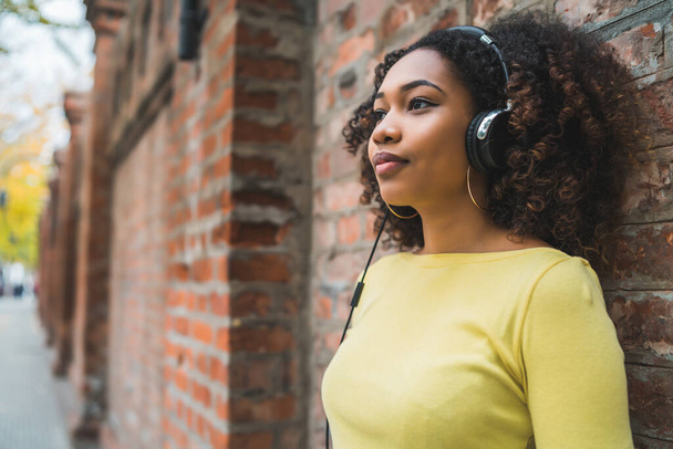 Πορτρέτο της νεαρής Αφρο-Αμερικανίδας που ακούει μουσική με ακουστικά στο δρόμο. Εξωτερικές πόρτες. - Φωτογραφία, εικόνα